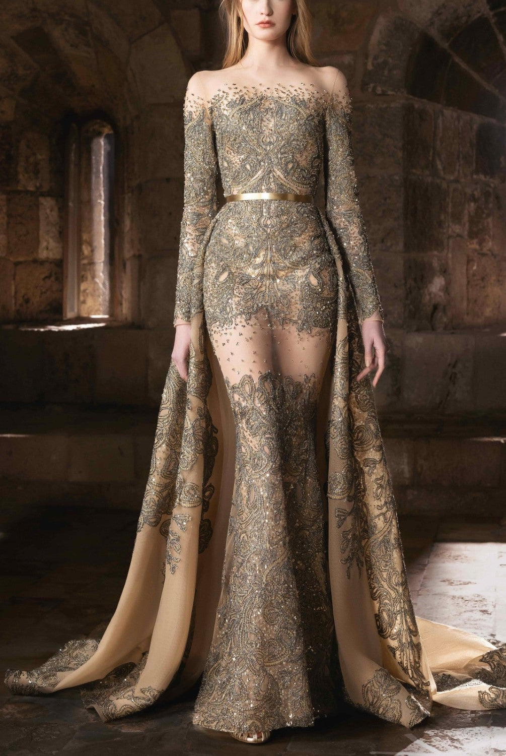 A sheer gold embroidered gown with an illusion neckline and an ethereal cascading train