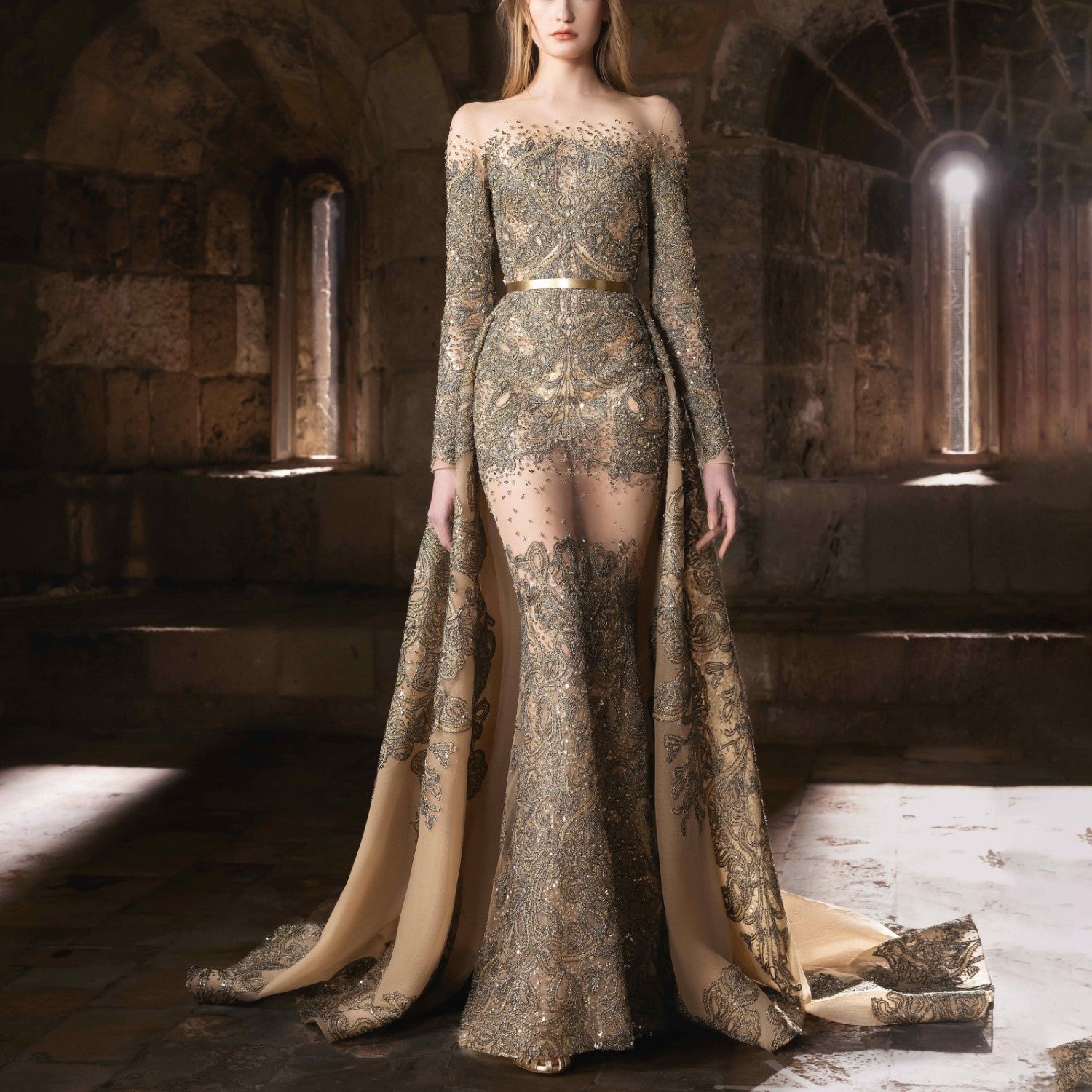 A sheer gold embroidered gown with an illusion neckline and an ethereal cascading train